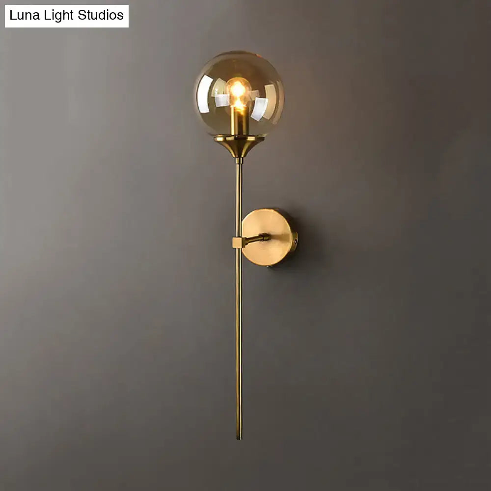 Modernist gold-toned glass round sconce lamp with spherical amber globe and slender stem for living room lighting