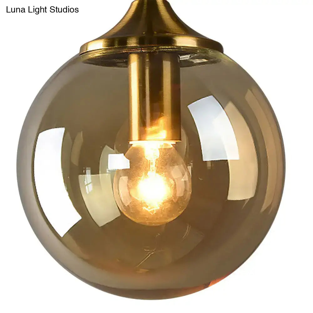 Modernist round sconce lamp featuring a warm amber glass globe with brass metal fixture and exposed filament bulb