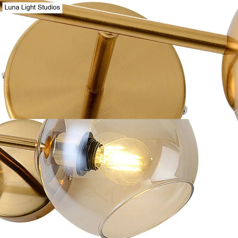 Modernist gold wall lamp with glass shade featuring a spherical smoked glass and exposed filament bulb for living room