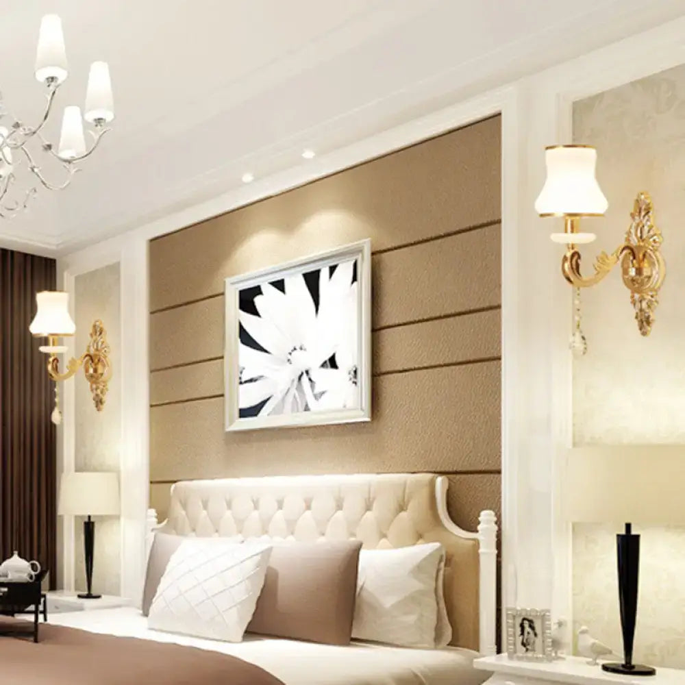 Cream-colored tufted bedhead with white frame alongside modernist gold wall sconce with glass shade direct wired electric