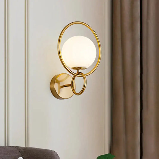 Modernist gold wall sconce with a circular frame and white glass shade for bedroom lighting