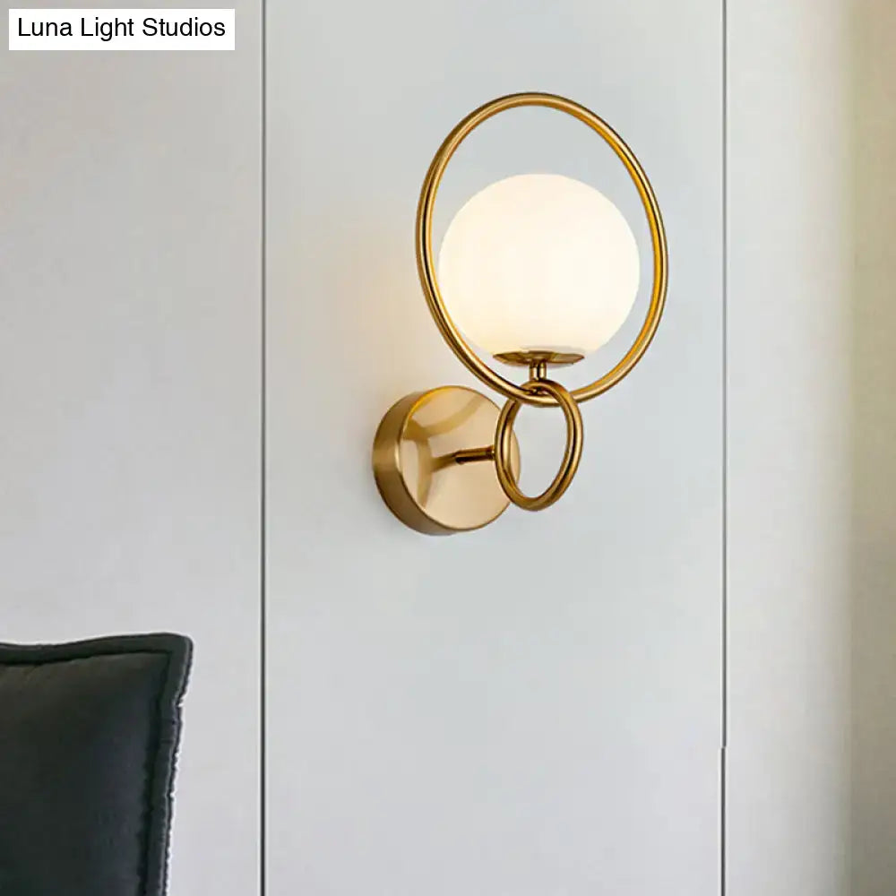 Modernist gold wall sconce featuring a white glass shade with frosted globe and interlocking circular rings for bedroom