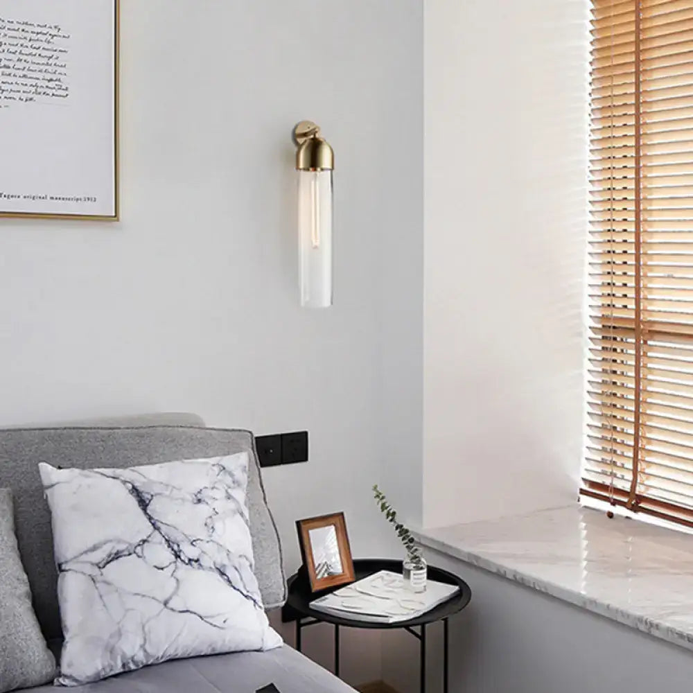 A sleek brass-finished modernist tube sconce light with clear glass and exposed filament bulb for bedroom use