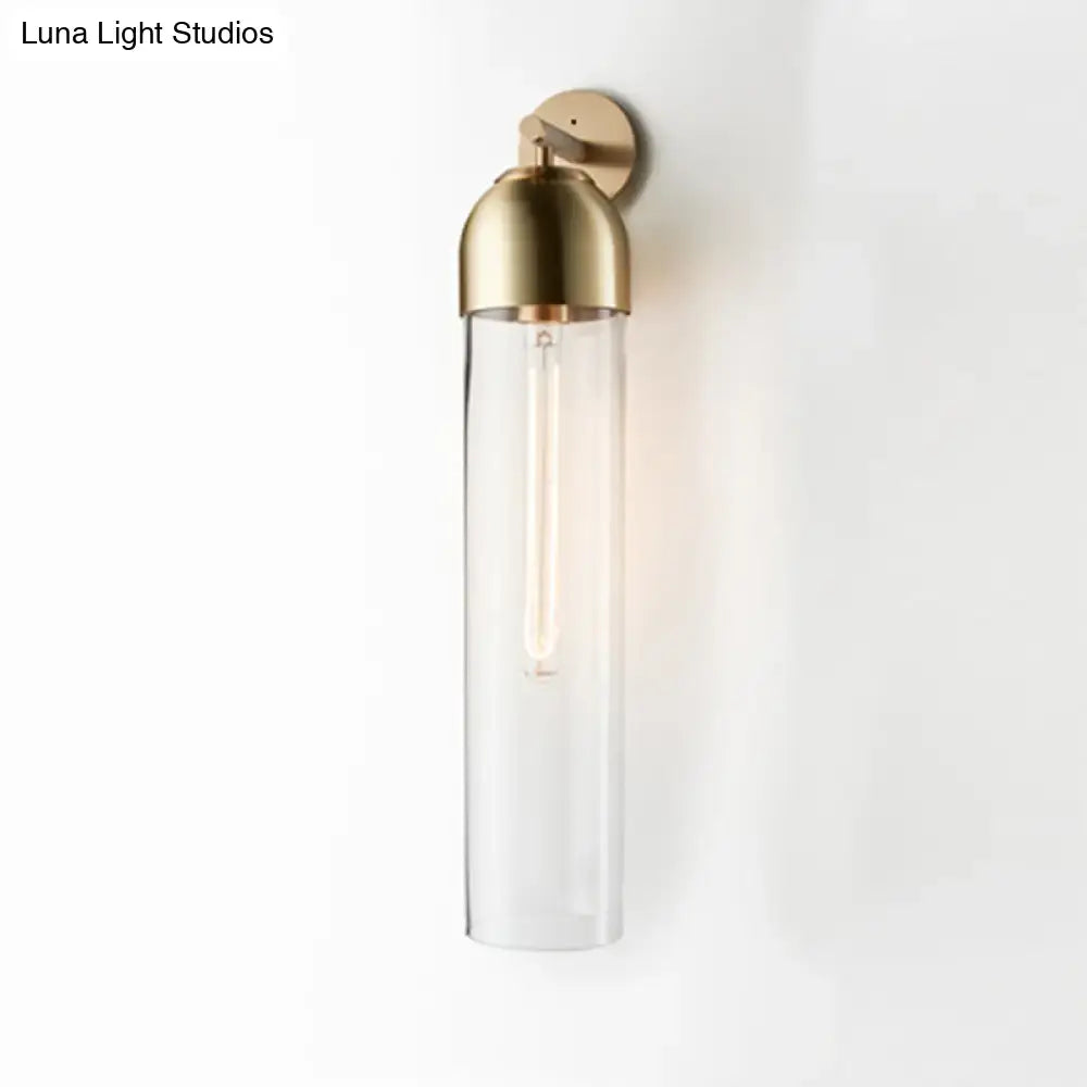 Modernist brass finished tube sconce light with clear glass cylinder and exposed filament bulb for bedroom use