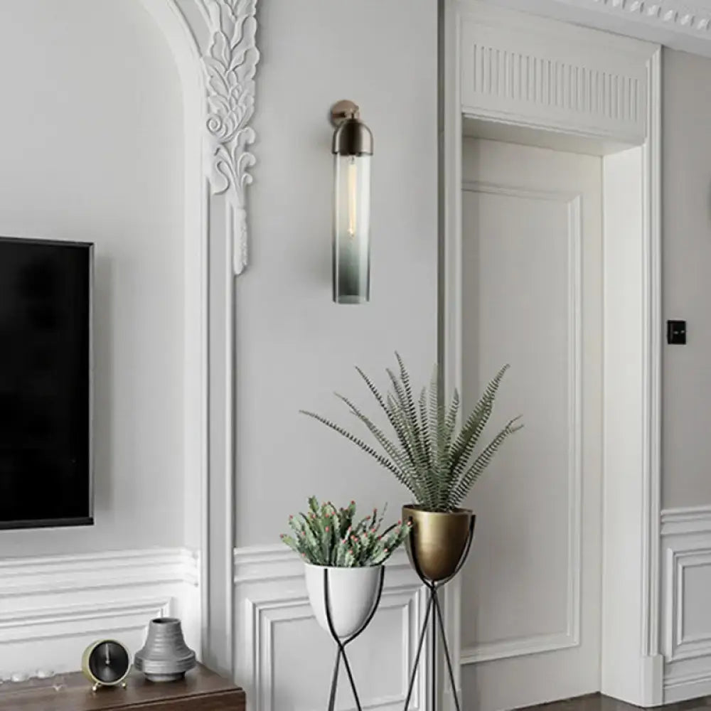 Modernist metallic tube sconce light with brass finish and clear glass body mounted on a curved arm for bedroom use