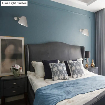 Black leather headboard with curved top and tufted design beneath modernist off-white and gold wall mounted sconce light with wide flare