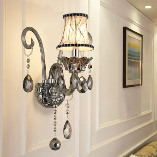 Silver-toned smoke grey crystal sconce with textured beige lampshade and faceted teardrop crystals for living room wall mounted lighting