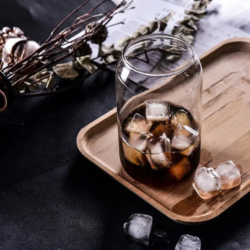 Clear glass motivational engraved shape beer glass cup filled with dark iced beverage on wooden tray