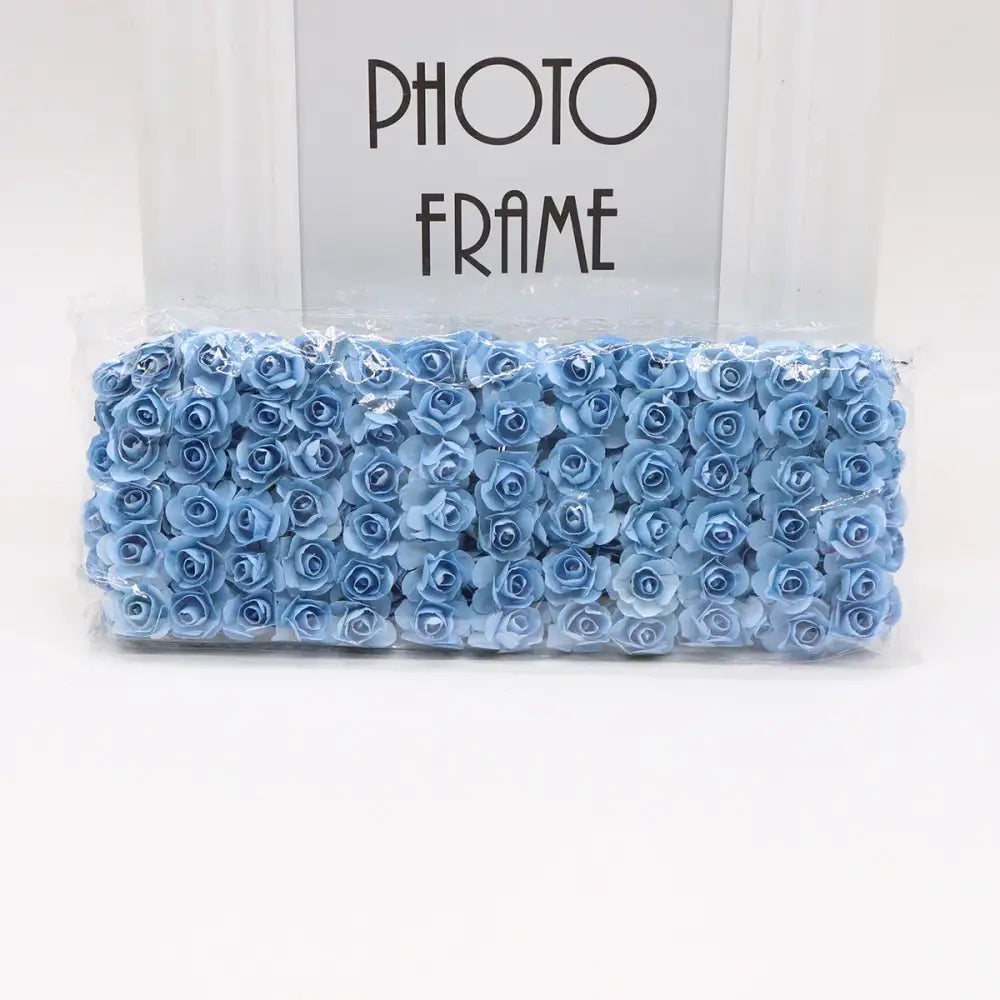 A package of light blue decorbites 144pcs 2cm artificial paper roses neatly arranged and sealed in clear plastic packaging
