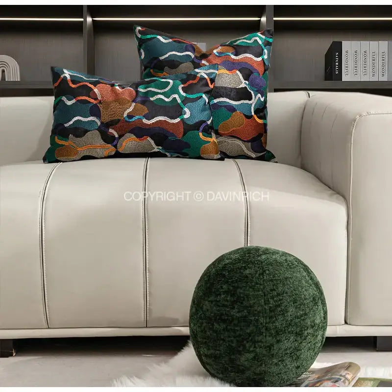 Two rectangular cushion covers with multicolor geometric embroidery abstract patterns on a dark base fabric atop a beige sofa