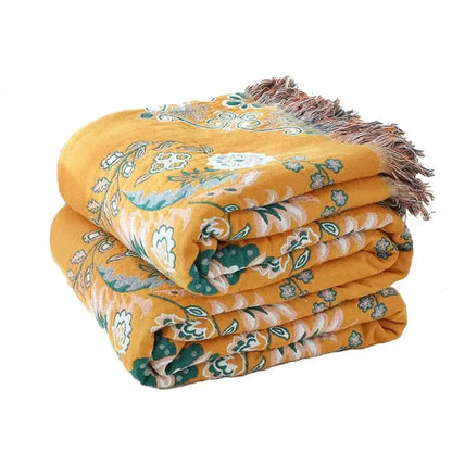 A mustard-yellow cotton throw blanket with decorbites gauze flowers pattern and fringed edge for stylish decor