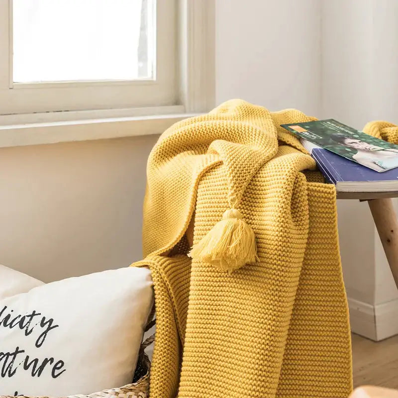 A cozy mustard yellow knit pompom tassel throw blanket with textured weave and matching tassel decorbites knit pompom