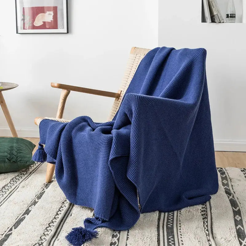 A rich navy blue decorbites knit pompom tassel throw blanket with textured weave and matching tassels on wooden chair