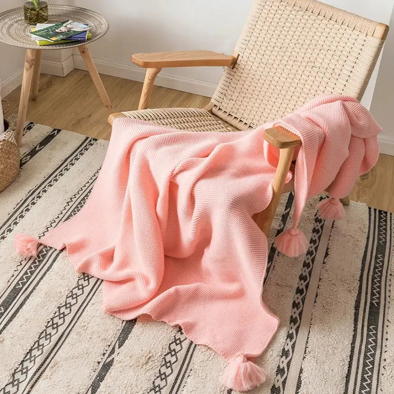 A soft pink knitted throw blanket with knit pompom tassels at each corner for decorbites knit pompom bedroom decor