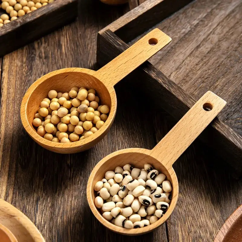 Two light brown natural beech wood tablespoons holding yellow soybeans and black eyed peas coffee scoop set