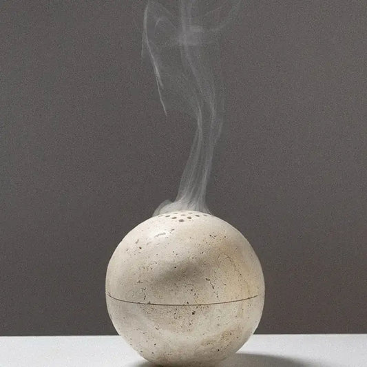 Natural beige travertine sphere incense burner with textured surface and perforations emitting smoke for living room decorbites beige travertine