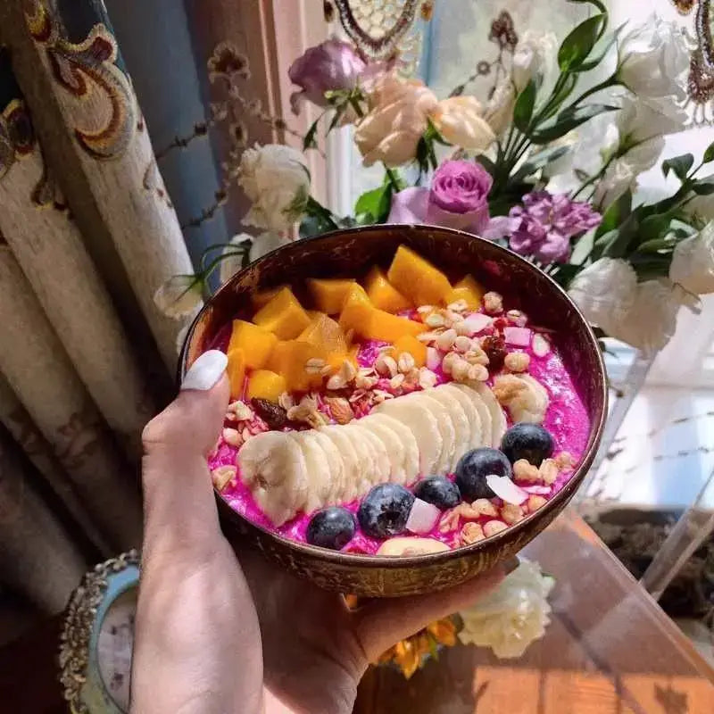 A vibrant pink acai bowl with mango, banana, blueberries, and granola in a natural dark brown decorbites coconut bowl set
