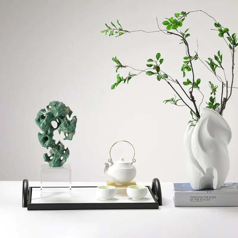 White ceramic teapot with gold handle on black tray beside cups, complementing decorbites green taihu stone coral sculpture decor