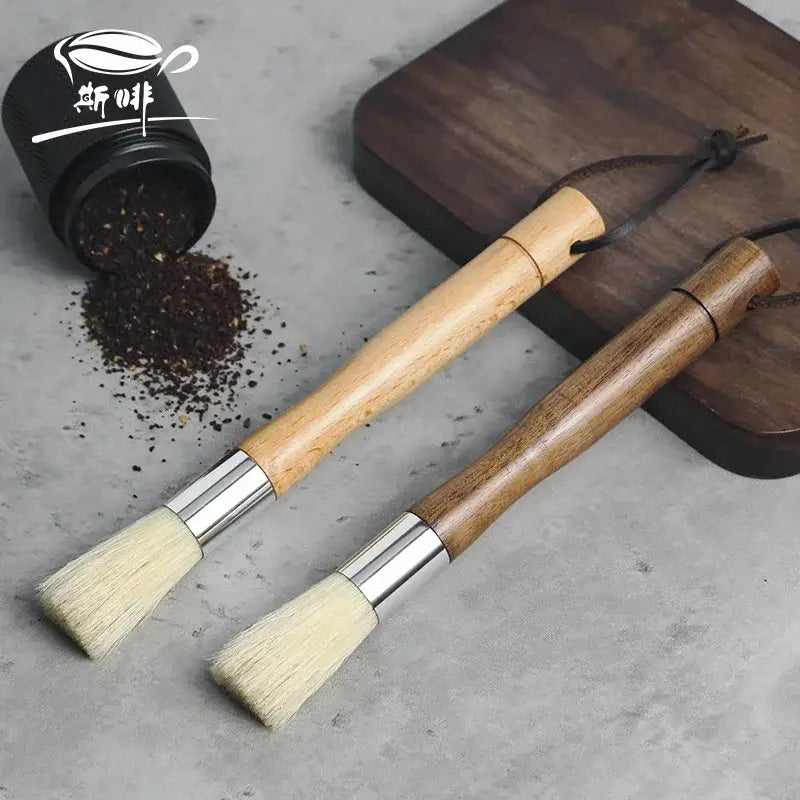 Two wooden-handled coffee grinder cleaner brushes with silver ferrules and light bristles beside loose-leaf tea container