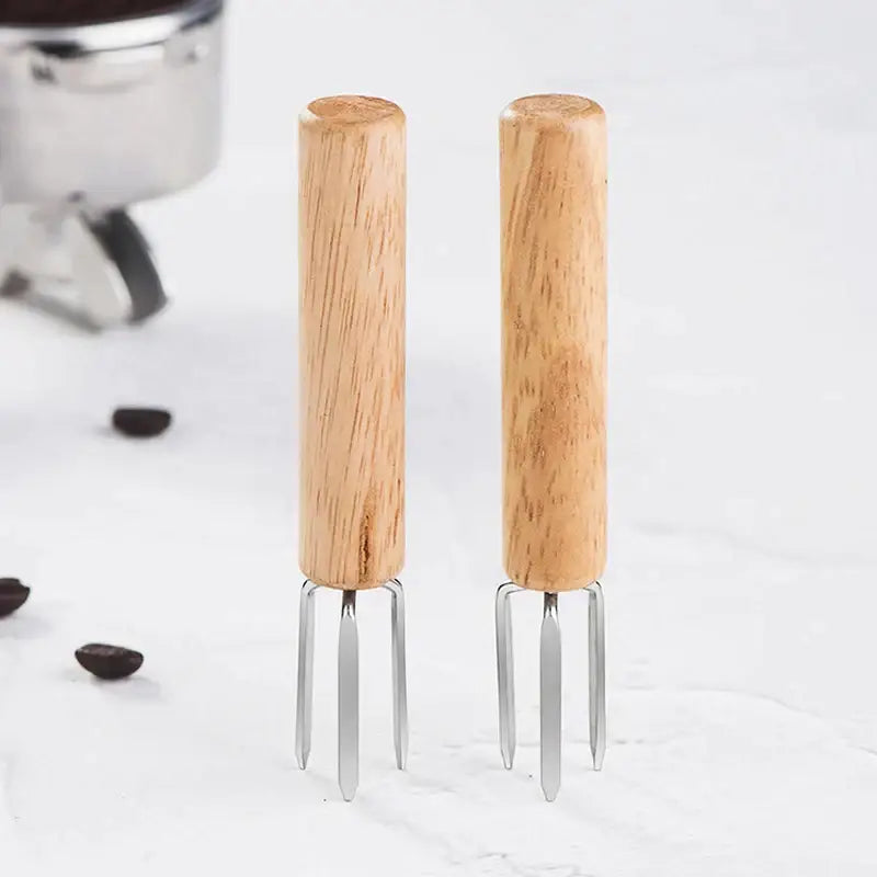 Two light-colored wooden-handled decorbites espresso stirrer with slender metallic prongs natural wood three prong espresso stirrer