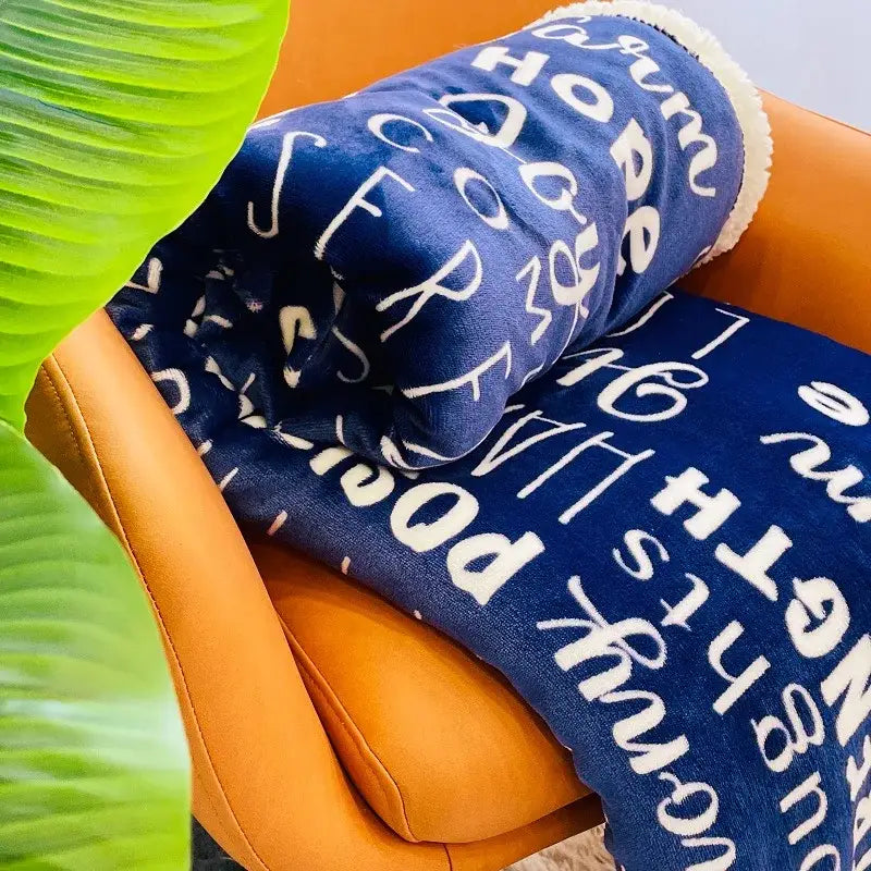 A decorbites cozy printed navy and cream cozy printed flannel blanket with white lettering draped over an orange chair
