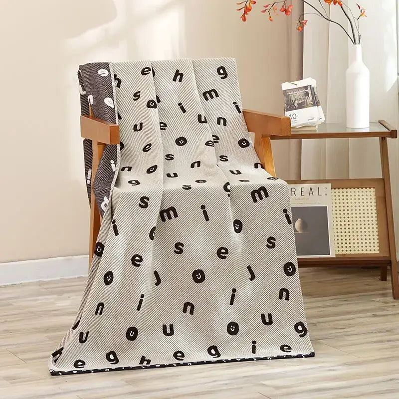 Beige cotton gauze throw blanket with black letters and smiley patterns draped on wooden chair for decorbites cat bath towel use