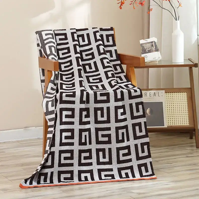 Navy blue gold hibiscus cat bath towel with black and white geometric pattern and orange border draped over wooden chair