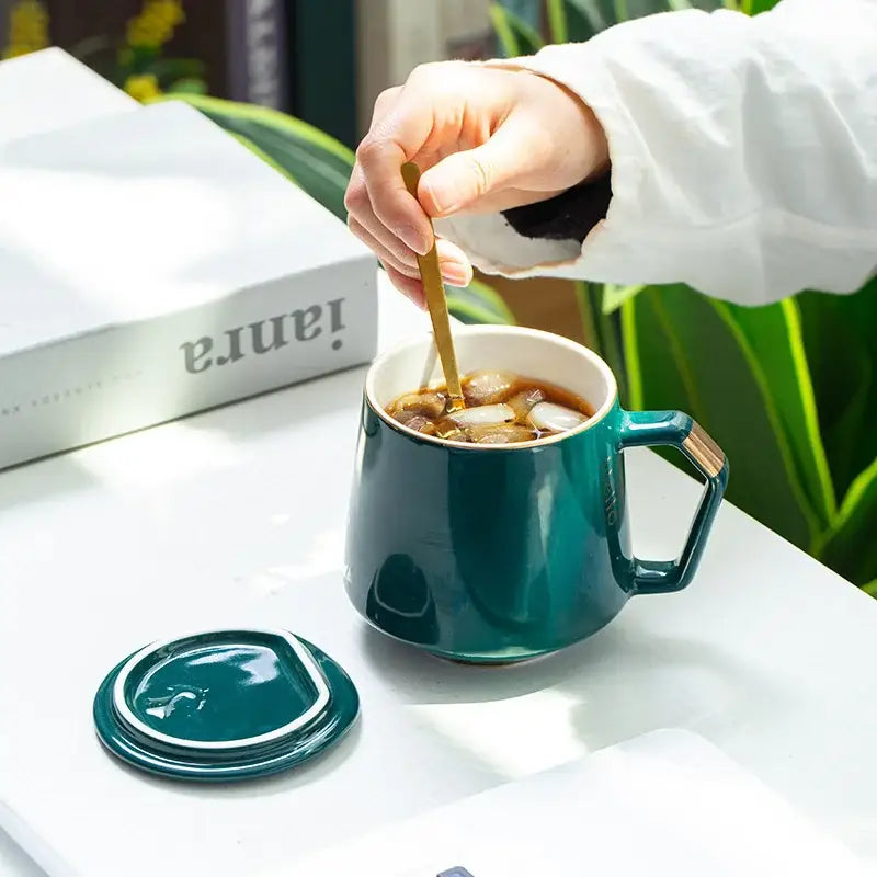 Teal ceramic mug with hexagonal handle and matching lid from navy and emerald ceramic mug set with gold spoons