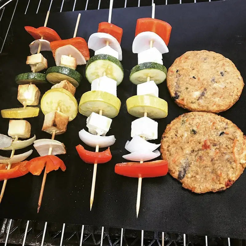 Three colorful vegetable skewers and plant-based patties cooking on a non-stick black bbq grill mat grill mat