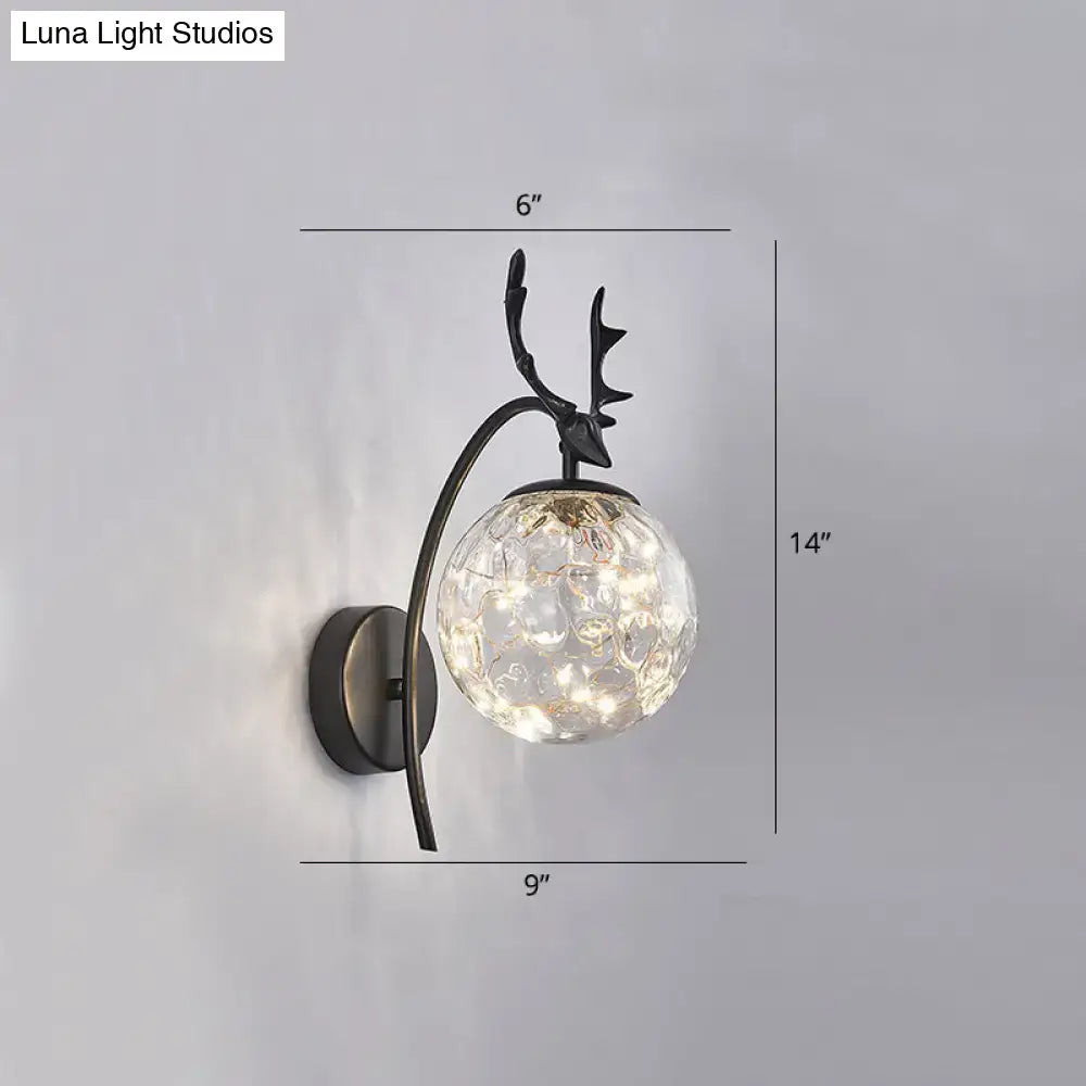 Antique brass-finished nordic ball wall mount sconce with clear textured glass globe and black deer antler design