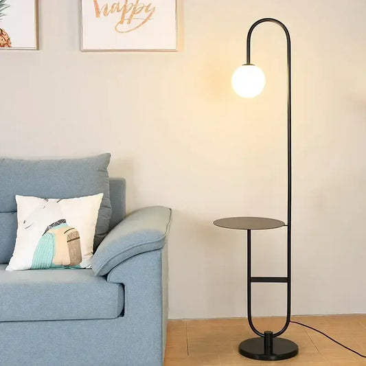 Black metal led floor lamp with curved stand, frosted glass globe bulb, and integrated round side table for living room
