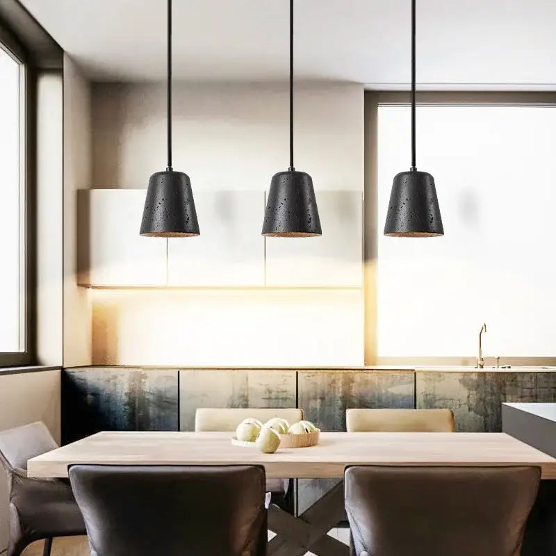 Three black travertine pendant lights with textured matte finish hang above dining table in warm LED interior