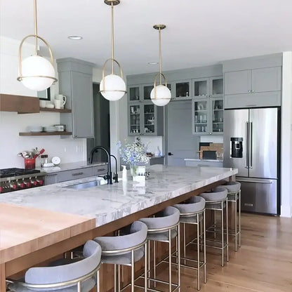 Nordic brass glass globe pendant light with white globe shades and brass frames hangs above marble kitchen island