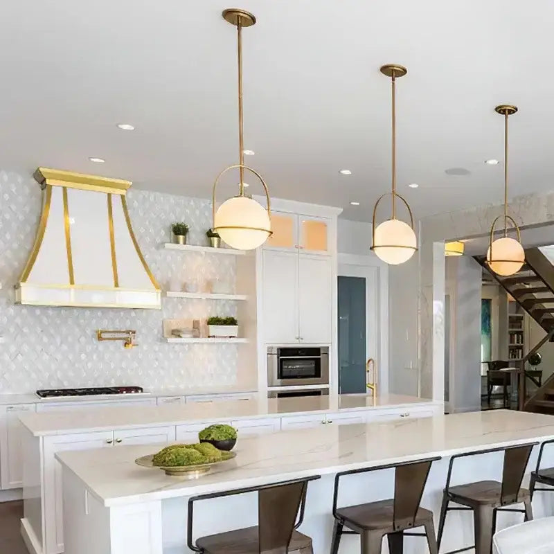 Three elegant nordic brass glass globe pendant lights with frosted shades hang above a modern kitchen island
