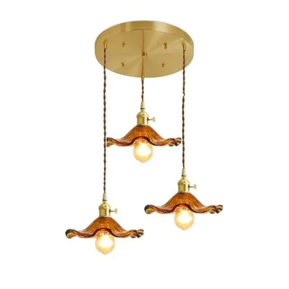 Brass-finished pendant light with three amber wavy glass shades and twisted copper chains for dining room use