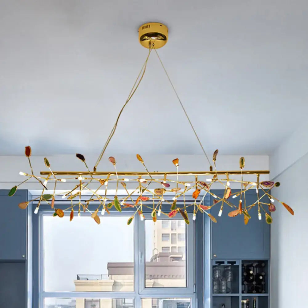 Gold-toned modern dining room ceiling light with colorful leaf-shaped glass accents and slender metal branches bulb base