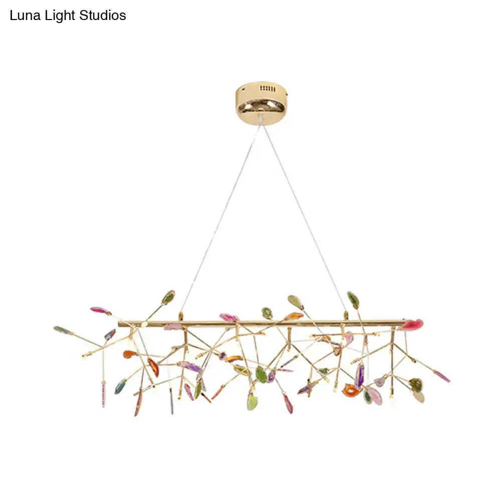 A modern gold-toned dining room ceiling light with colorful glass leaves on delicate branch bulb bases
