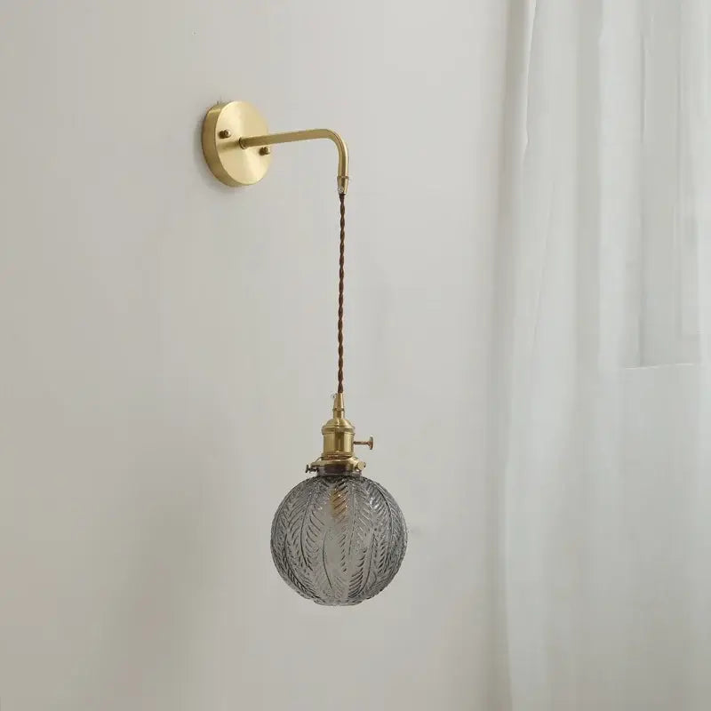Vintage-style wall sconce lamp with brass arm and gray etched glass globe hanging from braided cord for bedroom use