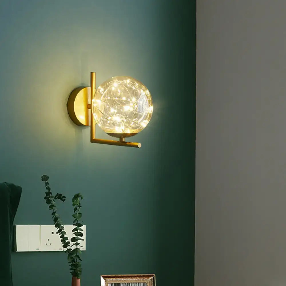 Nordic gold glass globe wall sconce featuring a gold-toned metal frame and warm fairy lights for bedroom decor
