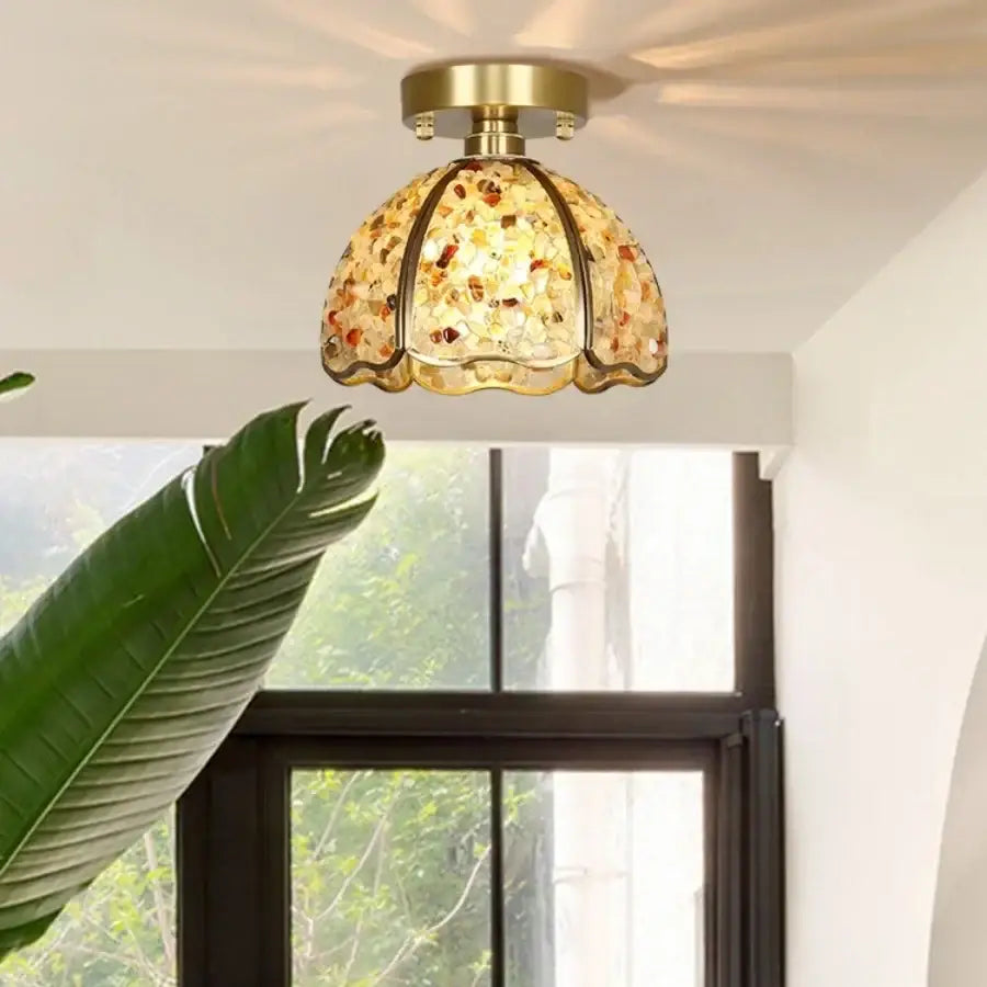 A brass-finished ceiling light with a green and purple glass crystal ceiling shade featuring amber and gold tones