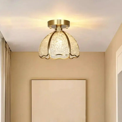 A gold-toned crystal ceiling light with a textured translucent glass shade shaped like a flower for bedroom use