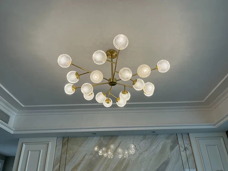 A modern brass dining room chandelier with multiple clear textured glass globe bulbs for indoor lighting