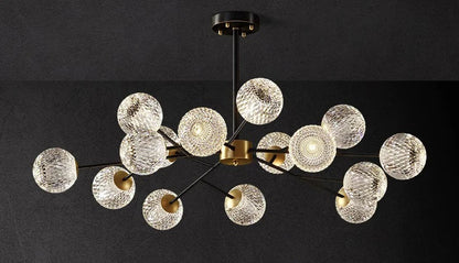 Modern chandelier with multiple clear textured glass spheres suspended by black metal arms on a brass fixture for indoor lighting