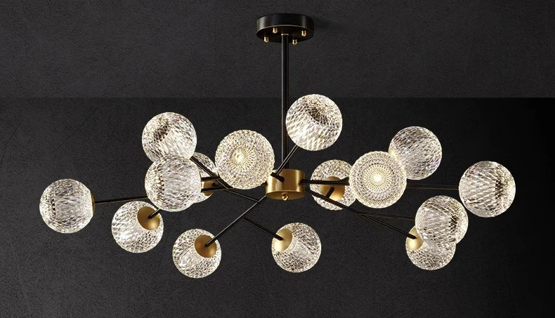 Modern chandelier with multiple clear textured glass spheres suspended by black metal arms on a brass fixture for indoor lighting