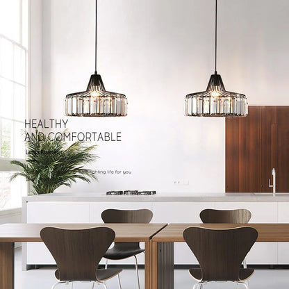 Two black-framed nordic led crystal pendant lamps with clear cylindrical accents hanging above a dining table