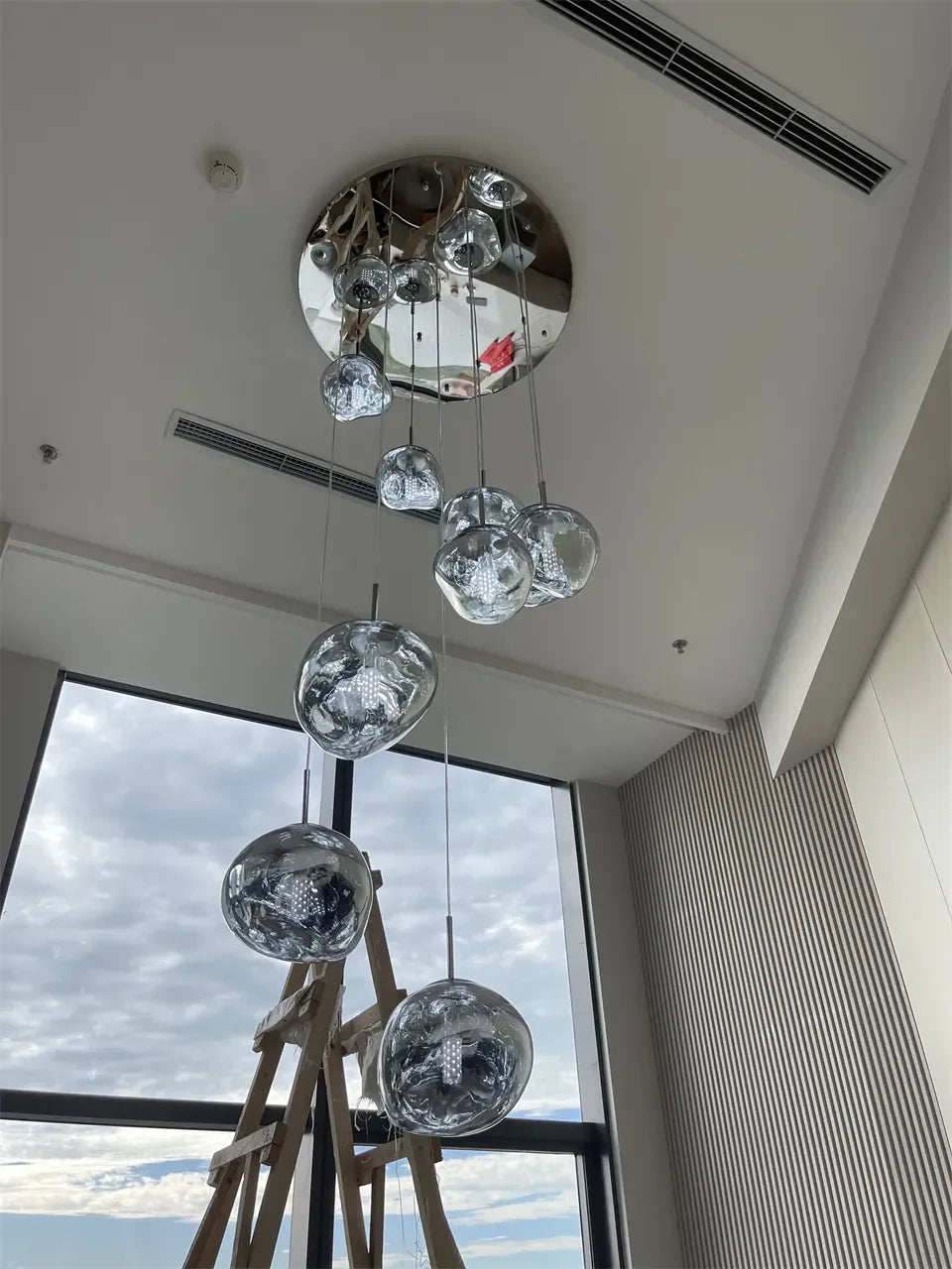 Modern chrome-finished spherical pendant light with clear glass globes hanging from circular mirrored base for indoor lighting