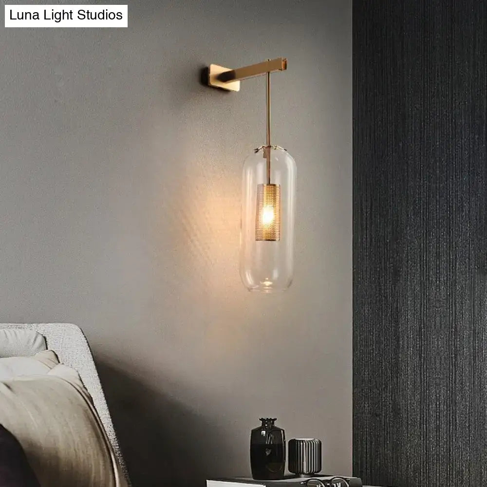A modern nordic decor brass and glass wall lamp with a clear glass lampshade and illuminated gold mesh bulb for bedroom