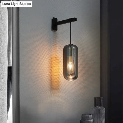 A sleek black metal nordic modern decor wall sconce with a cylindrical smoked glass lampshade and exposed filament bulb