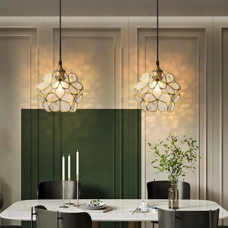 Two elegant gold-toned nordic modern petal acrylic pendant lamps with intricate glass shades hang above dining table