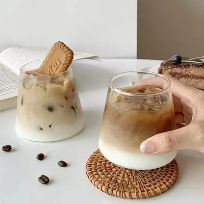 Clear glass iced coffee cup with frothy base and ice cubes held on woven coaster from nordic pink glass cocktail cups set decorbites glass cocktail